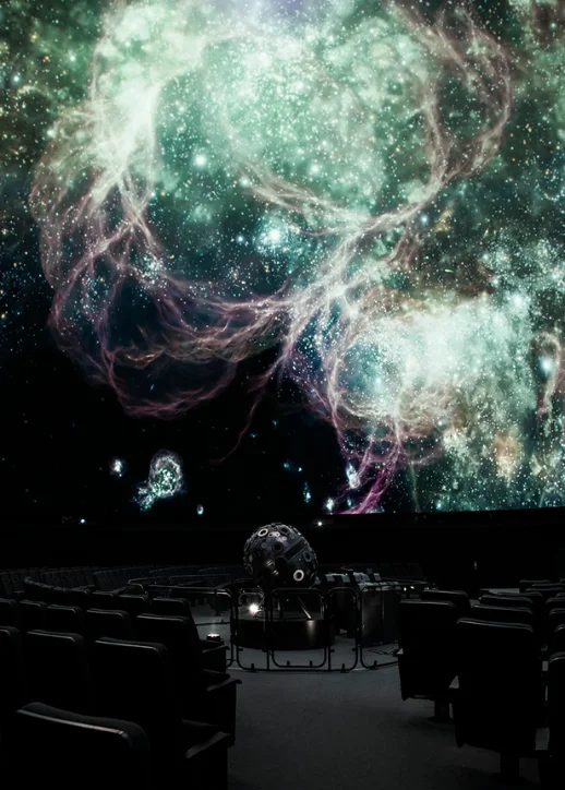 Ein großer Bildschirm zeigt eine beeindruckende Ansicht des Weltraums mit Sternen und Galaxien im Planetarium Berlin.