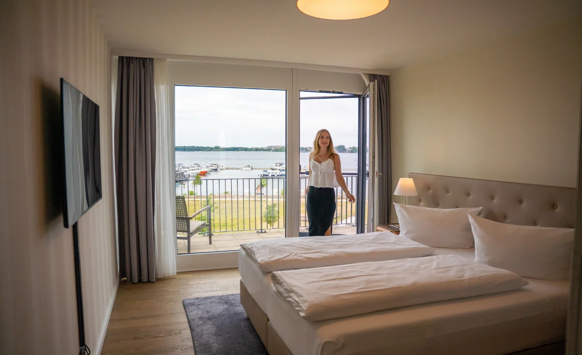 Eine Frau steht vor einem Bett in einem eleganten Zimmer im 5 Sterne Resort Müritz.