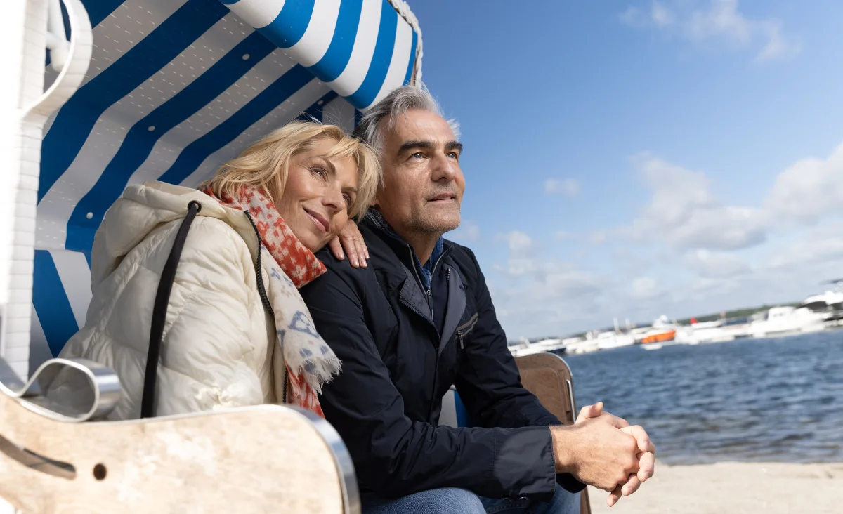 Ein Mann und eine Frau sitzen entspannt auf einer Liege am Strand des 5 Sterne Resorts Müritz.