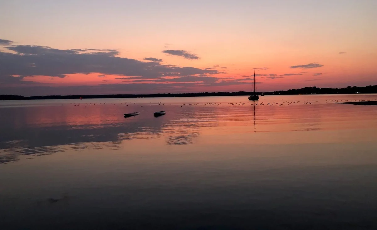Ein Boot schwimmt im Wasser bei Sonnenuntergang, umgeben von der malerischen Kulisse des 5 Sterne Resorts Müritz.