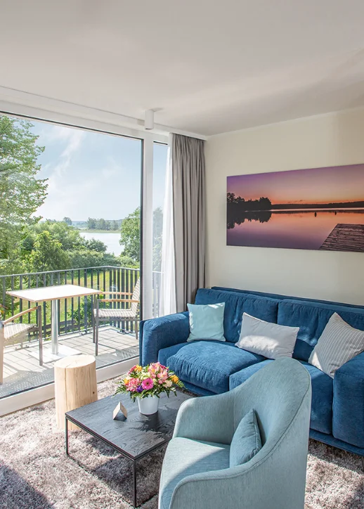 Ein Wohnzimmer mit einem blauen Sofa und einem großen Fenster, das viel Tageslicht hereinlässt.