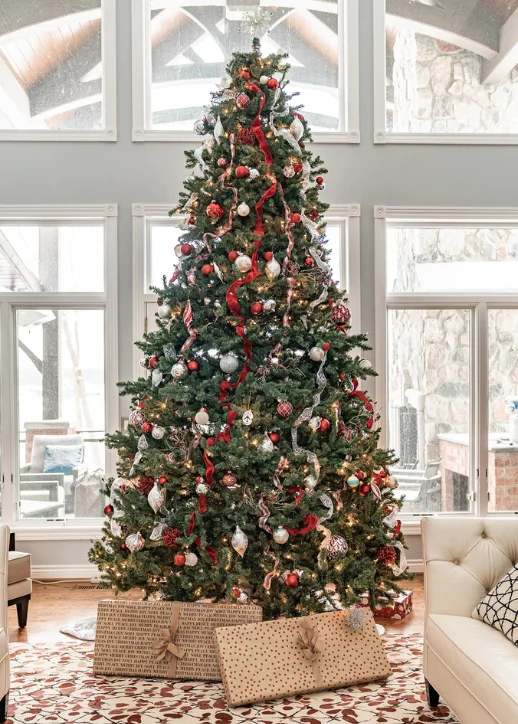 Ein großer Weihnachtsbaum von Tannenparadies Berlin steht in einem Wohnzimmer mit weißen Sofas, dekoriert für die festliche Saison.