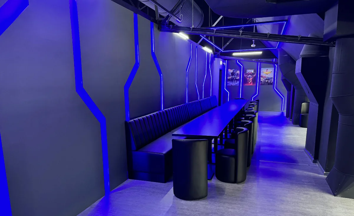 Moderner Lounge-Bereich mit blauer Beleuchtung und schwarzen Stühlen im Varpoint VR-Park, wo Abenteuer und Spaß auf Sie warten.