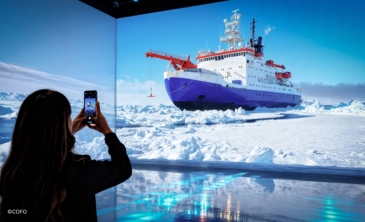 Eine Frau fotografiert ein Schiff auf einem Eisfeld während der Ausstellung "POLAR EXPERIENCE" in Berlin.