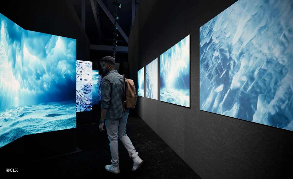 Ein Mann geht durch einen Raum mit großen Bildschirmen, die die POLAR EXPERIENCE über die Arktis und Antarktis zeigen.