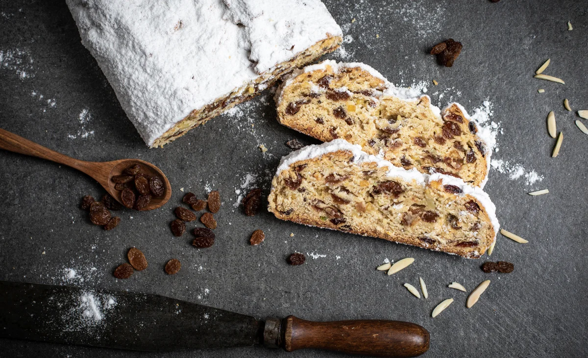Eine Scheibe Christstollen mit Nüssen und eine Tasse Kaffee auf einem Holzuntergrund, typisch für die Stollenbäckerei Krause.