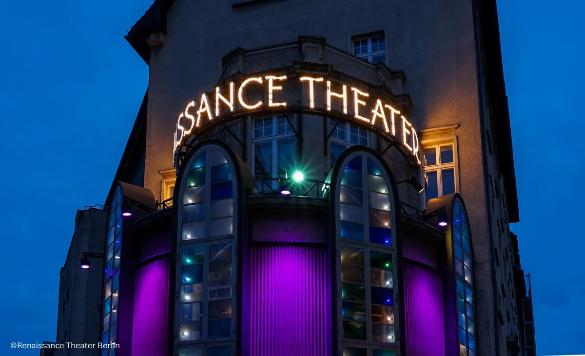 Eingang des Renaissance Theaters Berlin mit beleuchtetem Schriftzug und violett beleuchteten Fenstern in einem historischen Gebäude bei Dämmerung.