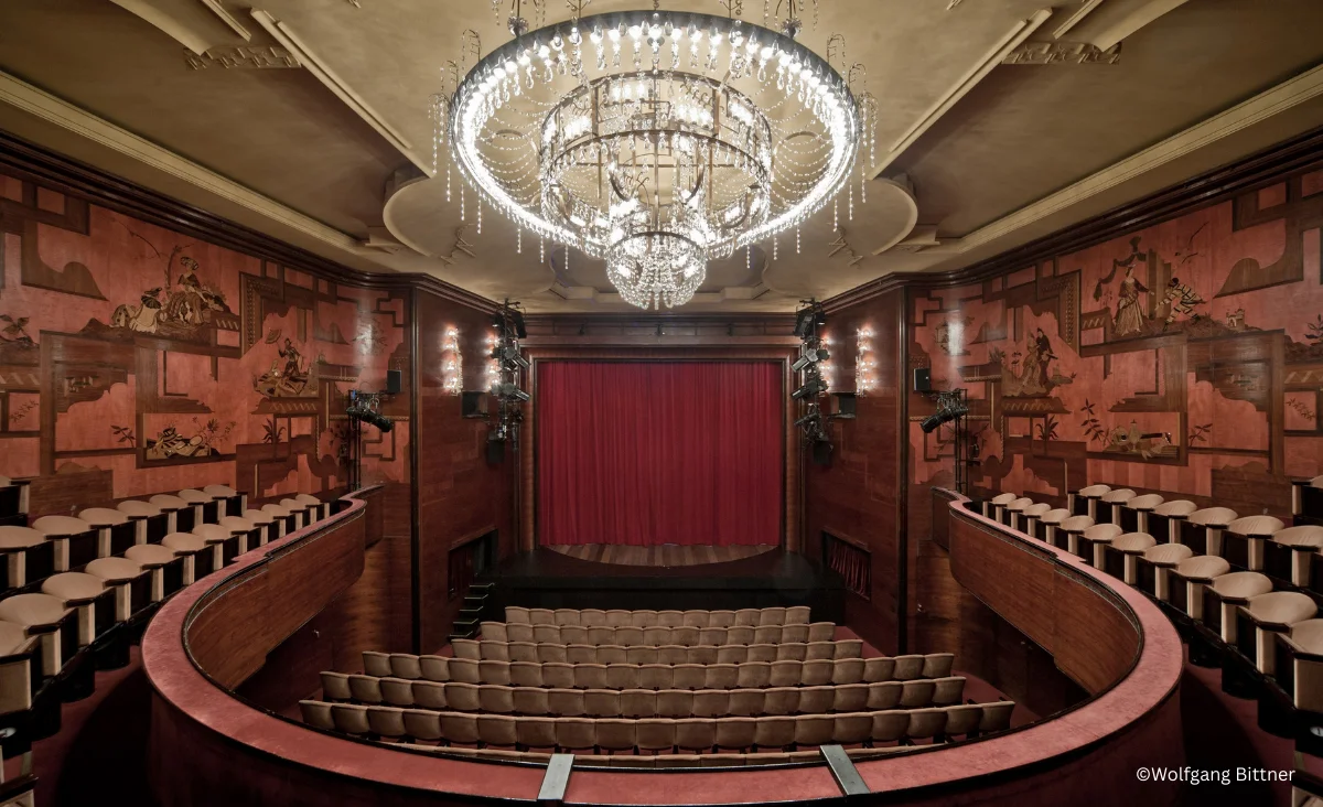 Innenansicht des Renaissance Theaters Berlin mit rotem Vorhang, geschwungenen Sitzreihen und großem Kronleuchter an der Decke