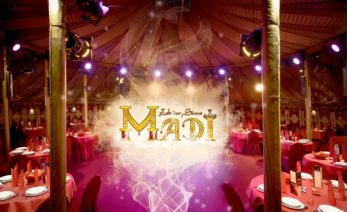 Blick in ein rundes, festlich gedecktes Restaurant mit Holzbalken und zentraler Lichtinstallation, darüber der Schriftzug 'MADI'