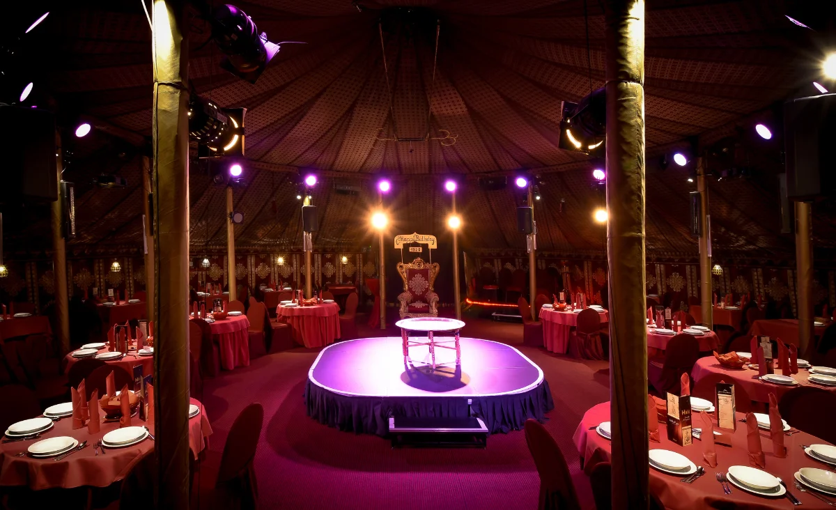 Zelt mit runden Tischen und roten Tischdecken, in der Mitte leuchtet der Schriftzug 'MADI' mit Rauch- und Lichteffekten