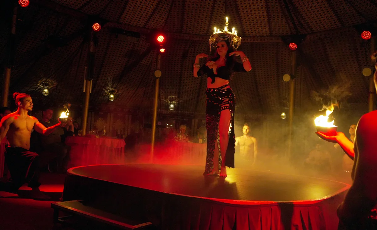 Feuershow mit einer Tänzerin auf einem runden Podest im Madi-Zelt der Sinne, umgeben von mehreren Männern mit brennenden Fackeln in den Händen.