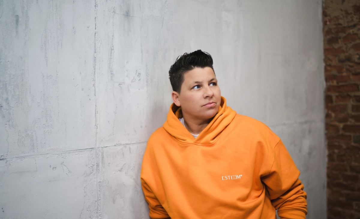 Kerstin Ott in einem orangefarbenen Hoodie lehnt entspannt gegen eine Wand bei der Veranstaltung 'SCHLAGERNACHT'26'.