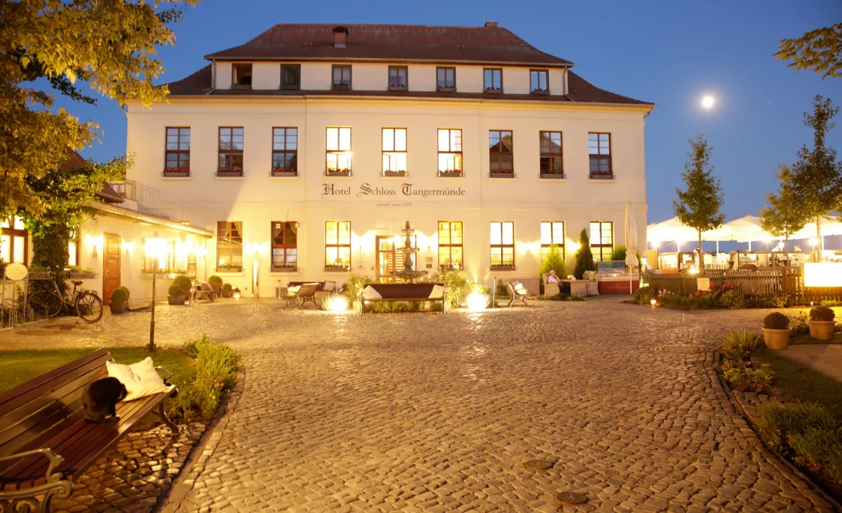 Beleuchtetes historisches Hotelgebäude mit gepflastertem Innenhof und Bäumen bei Abenddämmerung