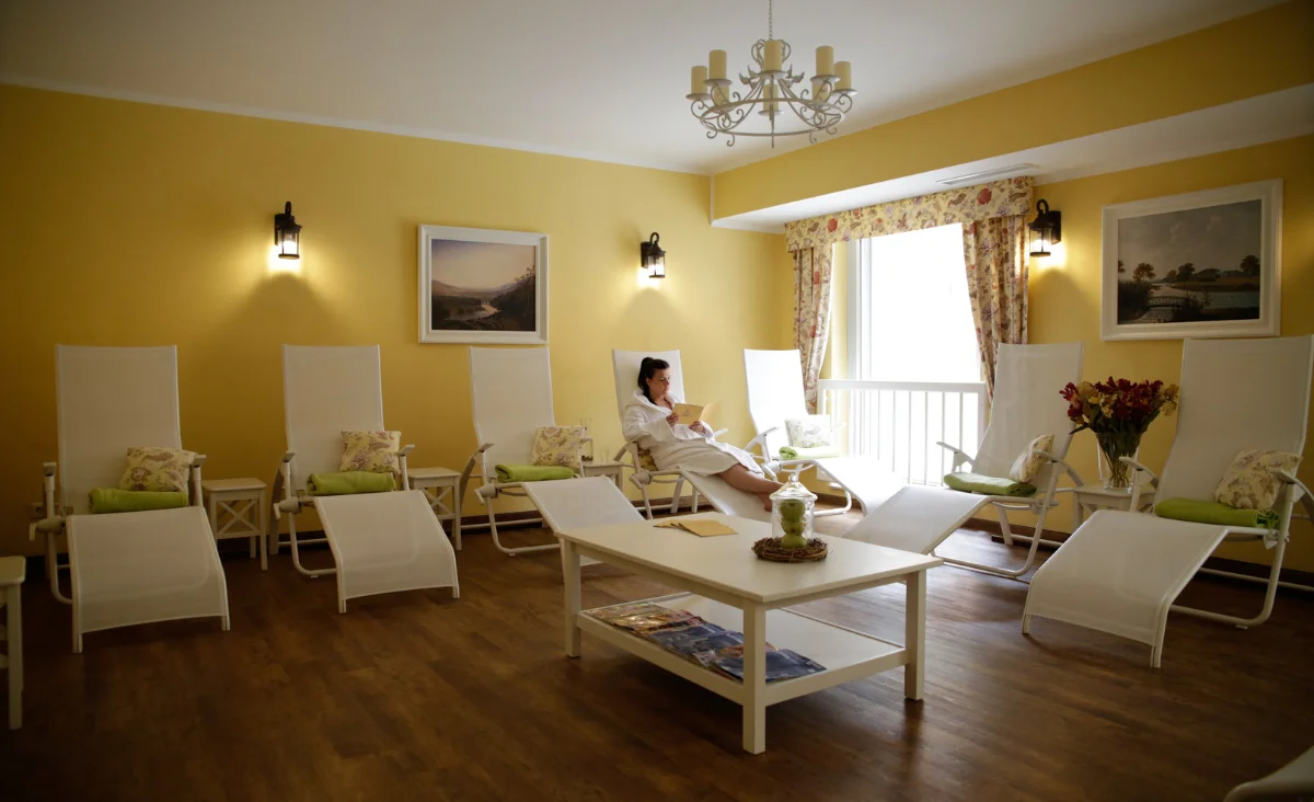 Ruheraum mit mehreren Liegestühlen, einem niedrigen Tisch in der Mitte und einer Person, die auf einem Liegestuhl sitzt.