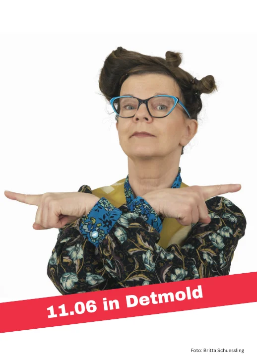 Eine Frau mit hochgestecktem Haar und gemustertem Oberteil zeigt mit beiden Händen nach rechts