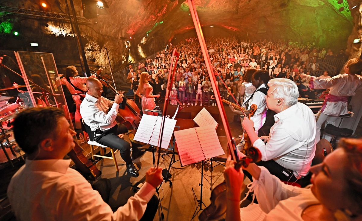 Eine Gruppe von Musikern spielt in einer Höhle, während eine begeisterte Menge zuschaut. Waterloo - The ABBA Show.