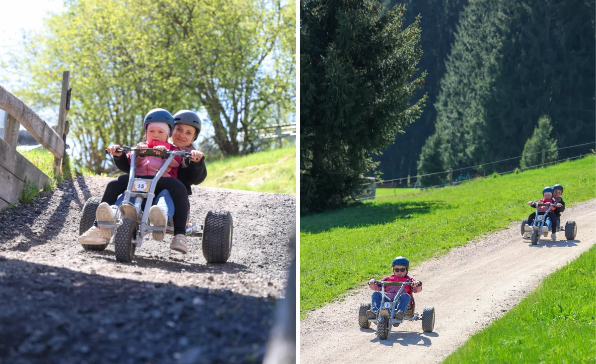 Zwei Kinder mit blauen Helmen fahren nebeneinander auf vierrädrigen Tretfahrzeugen einen geschotterten Weg hinab. Im linken Bildausschnitt ist eine Nahaufnahme der beiden Kinder zu sehen, die auf einem abschüssigen Abschnitt fahren, flankiert von einem Holzzaun und grünem Gras. Im rechten Bildausschnitt sind die Kinder aus größerer Entfernung auf einem breiten, hellen Schotterweg zu erkennen, der durch eine grüne Wiesenlandschaft mit Bäumen führt. Die Szene spielt in Wurzelrudis Erlebniswelt.