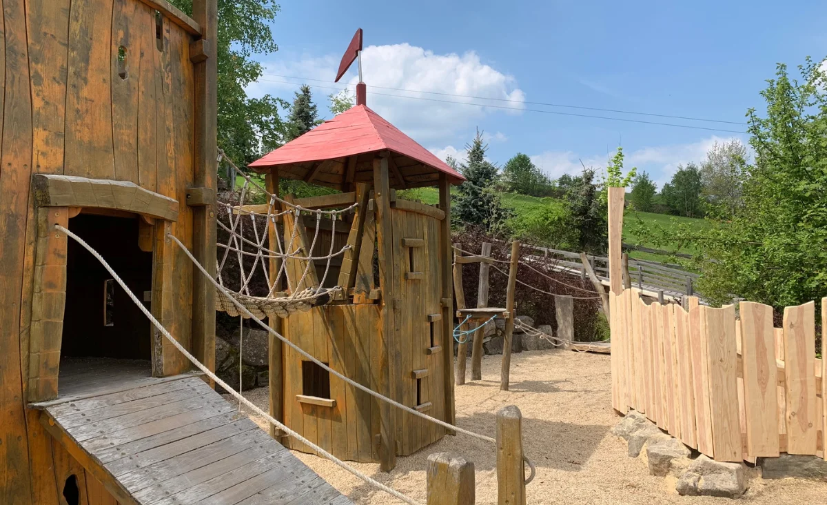 Spielbereich aus Holz mit rotem Dach und Rutschen in Wurzelrudis Erlebniswelt.