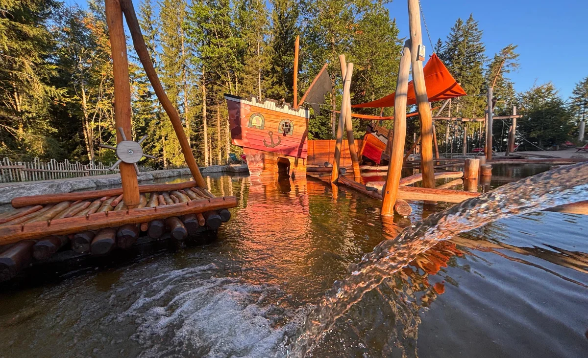 Wasserpark Wurzelrudis Erlebniswelt mit einer Rutsche und einer Holzbrücke, die zum Spielen einlädt.