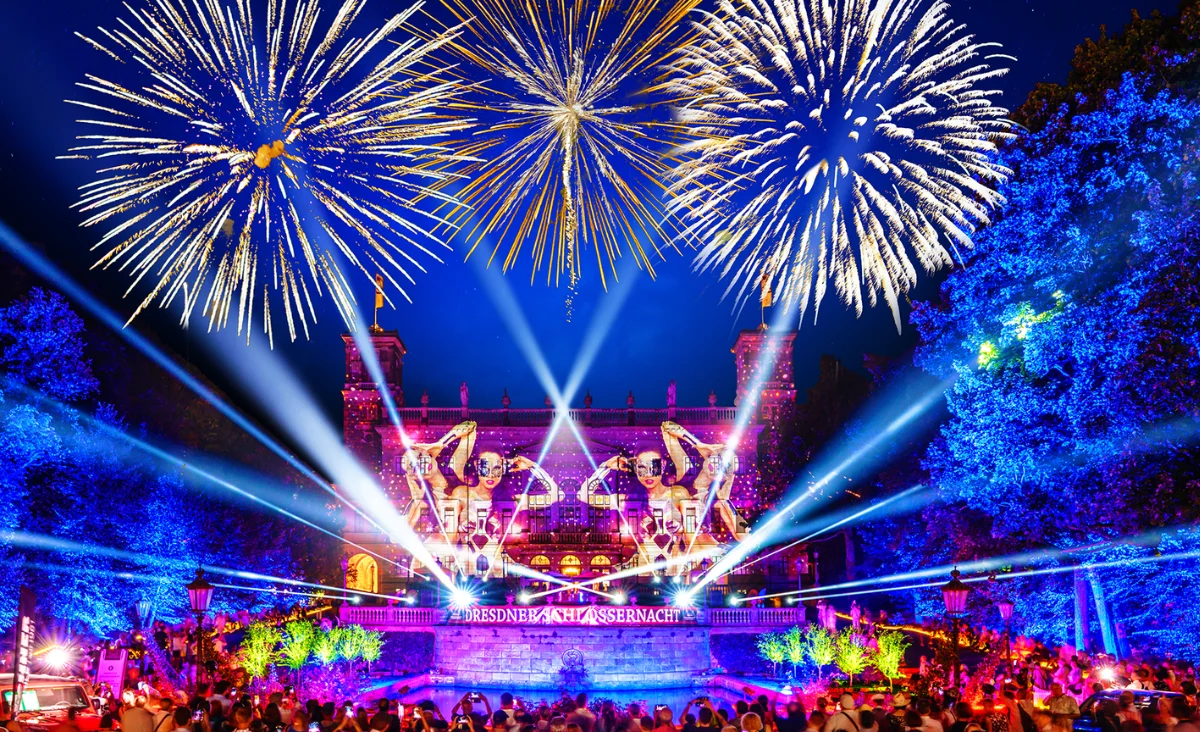 Feuerwerk und Lichtstrahlen über einem historischen Schloss mit beleuchteten Bäumen und einer Menschenmenge bei der Dresdner Schlössernacht.