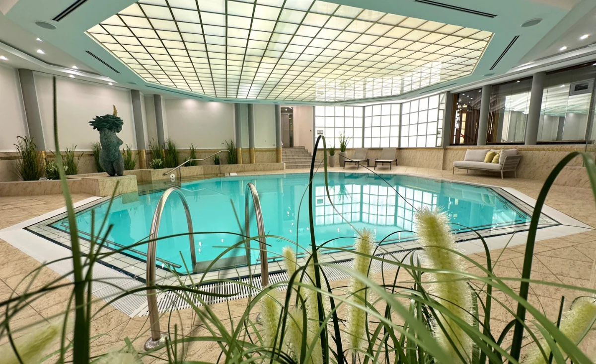Innenaufnahme des rechteckigen Schwimmbeckens im Hotel Kaiserhof Heringsdorf mit Glasdach, Pflanzen und Sitzgelegenheiten