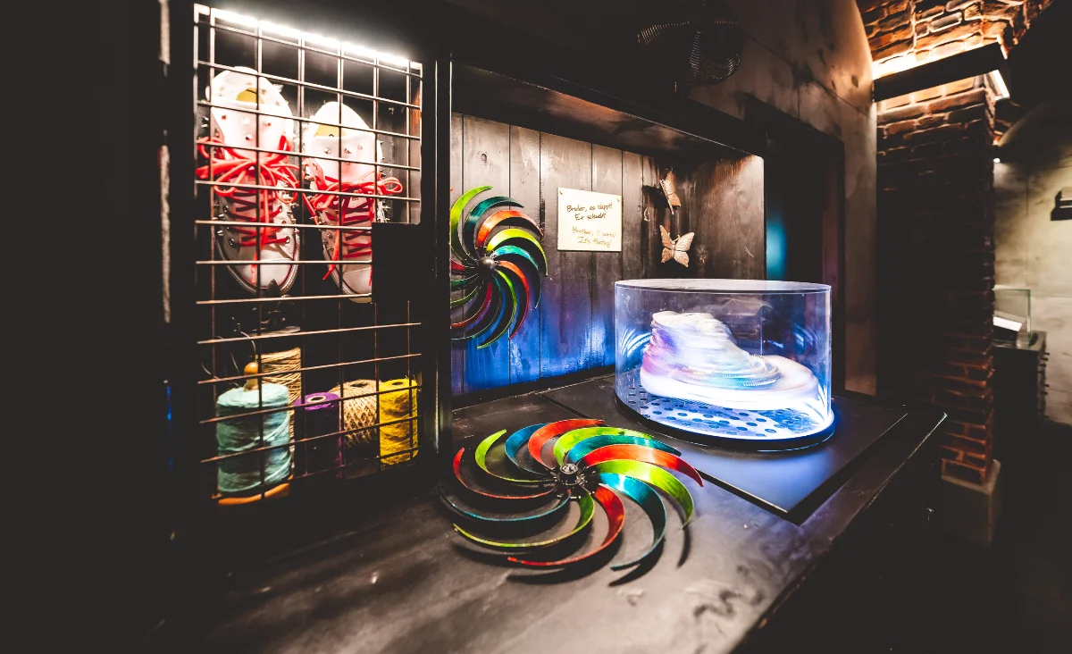 Detailaufnahme eines magischen Schuhs unter einer transparenten Haube auf einem Tisch mit bunten, spiralförmigen Dekorationen
