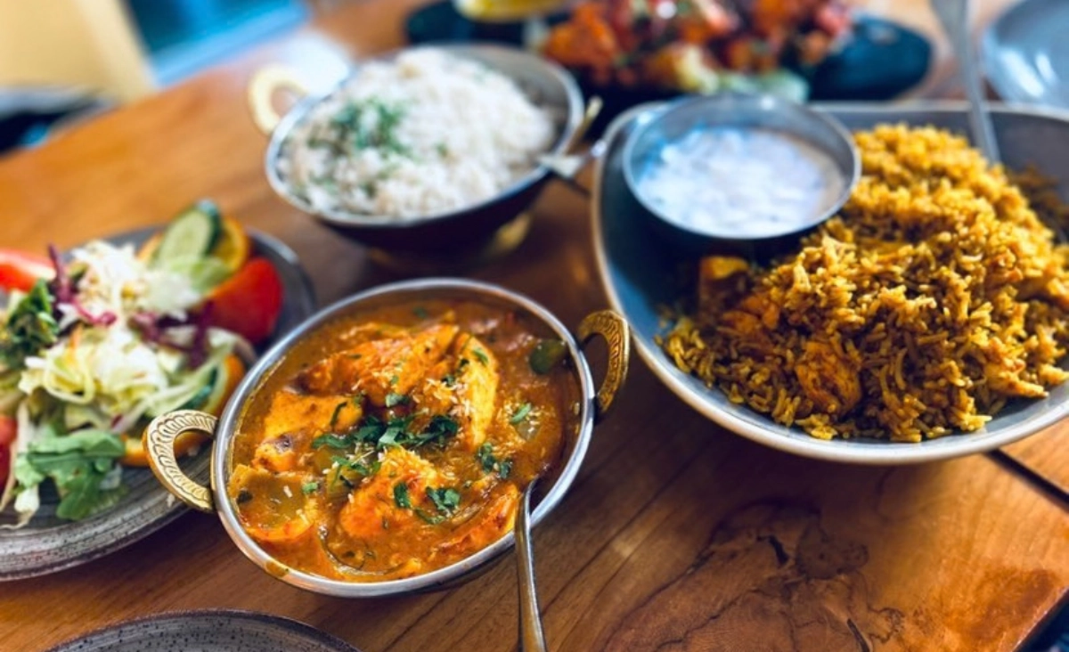 Teller mit indischem Currygericht, Reis, Salat und Joghurtsoße auf Holztisch angerichtet