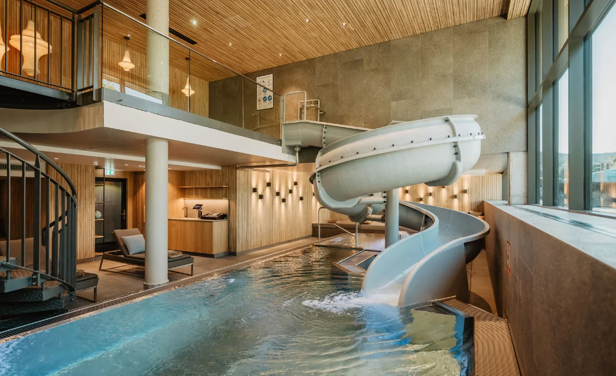Moderner Indoor Pool im Hotel Bodenmaiser Hof mit großer Kurven-Wasserrutsche und stilvollem Holzdesign